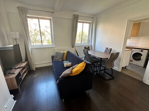 Ett kompakt bostadsutrymme med en soffa, ett matbord, en tv och en tvättmaskin.