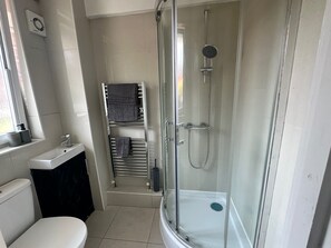 Ett modernt badrum med en dusch som är avskärmad med glasväggar, en toalett och en handduksställning.