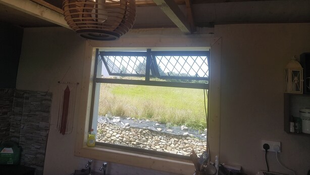 A kitchen with a window, a hanging light fixture, and a stone wall. - Tiny living on the Wild Atlantic Way (Tralee)