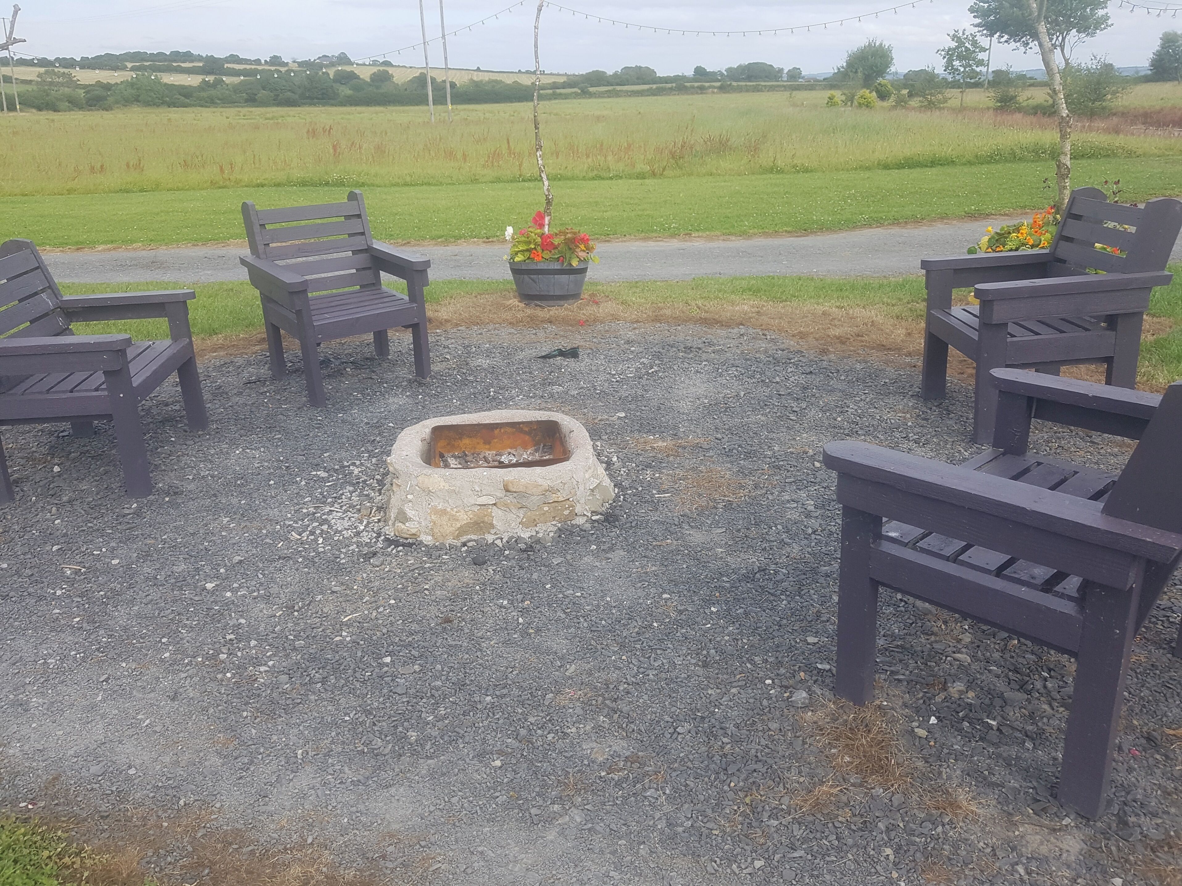 A gravel patio with a fire pit surrounded by wooden chairs.