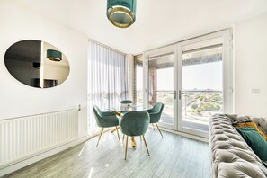 A modern living room with a round dining table, green chairs, a grey sofa, and a large window with a city view. - Top Floor Penthouse Near Stadium - Free Parking (London)
