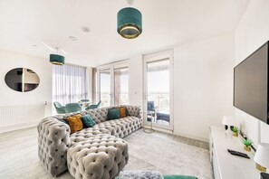 A modern living room with a tufted sofa, a round mirror, and a flat-screen TV. - Top Floor Penthouse Near Stadium - Free Parking (London)