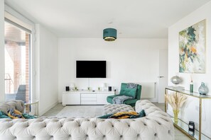 En moderne stue med en stor sofa med knapper, et fladskærms-tv monteret på væggen, en grøn lænestol og et sofabord i glas.