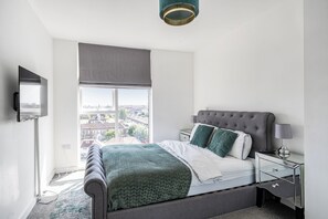 A bedroom with a bed, a nightstand, a lamp, a window with a view, and a ceiling light. - Top Floor Penthouse Near Stadium - Free Parking (London)