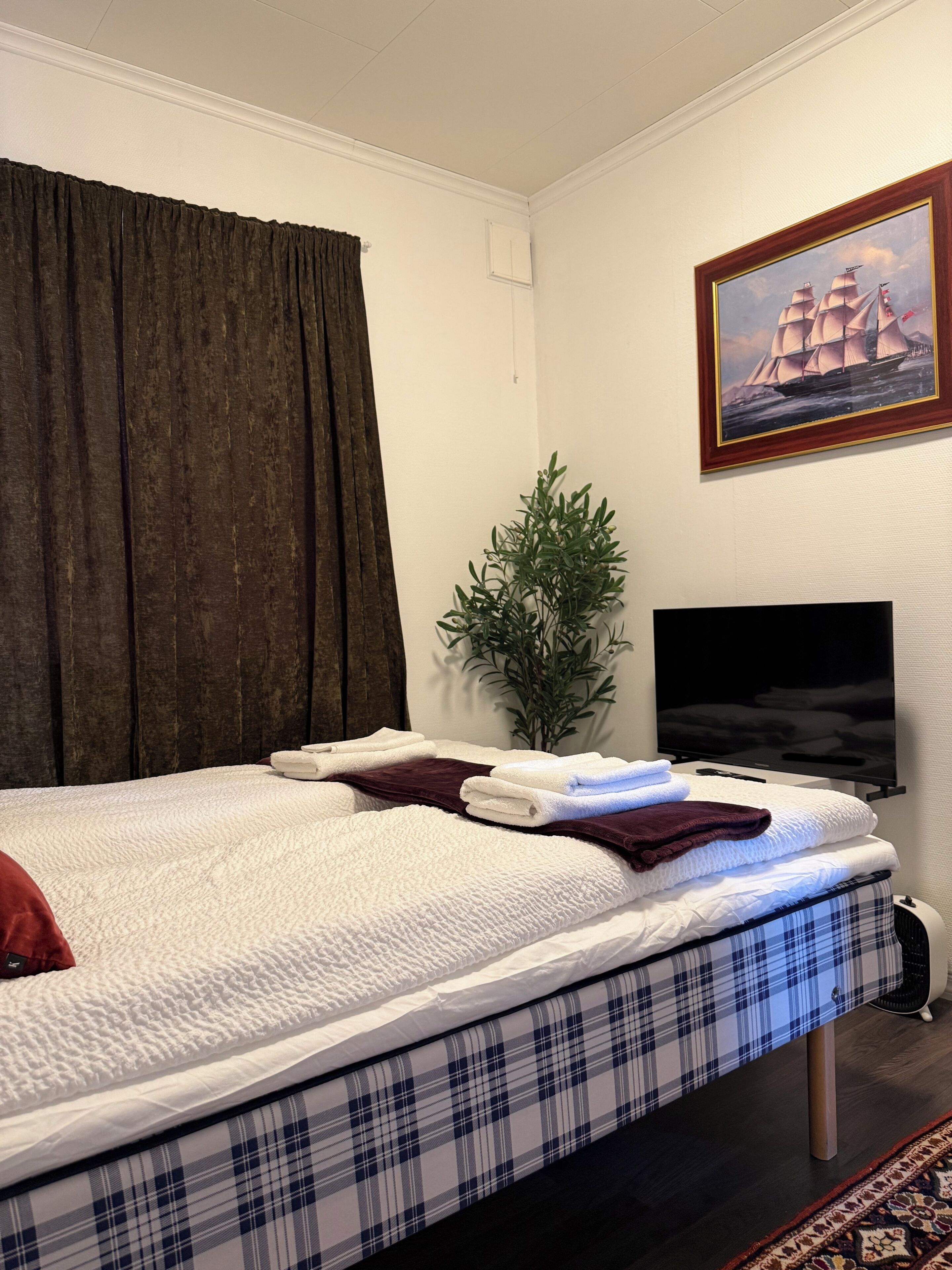 Ein Hotelzimmer mit einem Bett, einem Fernseher, einem Gemälde und einer Pflanze.