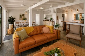 A spacious living area with a leather sofa, wooden coffee table, and a dining area with chairs and a table. - Cairns Beachfront Retreat (East Trinity)