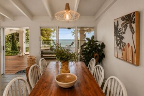 A dining area with a wooden table, white chairs, a large bowl, and a hanging light fixture. - Cairns Beachfront Retreat (East Trinity)