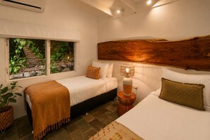 A room with two beds, a window with a view of greenery, a wooden headboard, and a bedside lamp. - Cairns Beachfront Retreat (East Trinity)