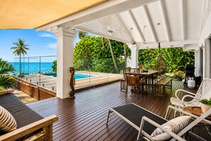 A wooden deck with a pool, outdoor furniture, and a view of the ocean. - Cairns Beachfront Retreat (East Trinity)