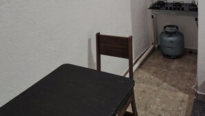 Pieni keittiönurkkaus, jossa on kaasuliesi, kaasupullo, tuoli ja pöytä.