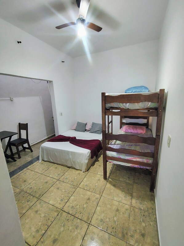 A small, compact room with a bunk bed, a single bed, a desk with a chair, and a ceiling fan.