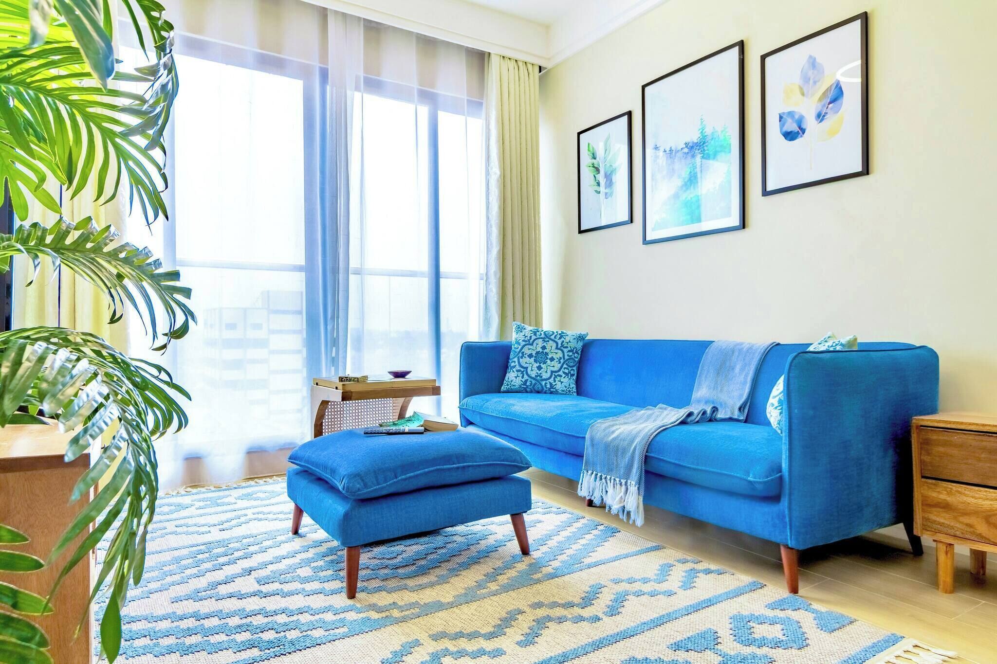 Una sala de estar con un sofá azul, un reposapiés a juego y una alfombra estampada.