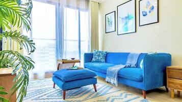 Una sala de estar con un sofá azul, un reposapiés a juego y una alfombra estampada.