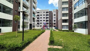 Et moderne lejlighedskompleks med en central gårdsplads, legeplads og en belagt sti.