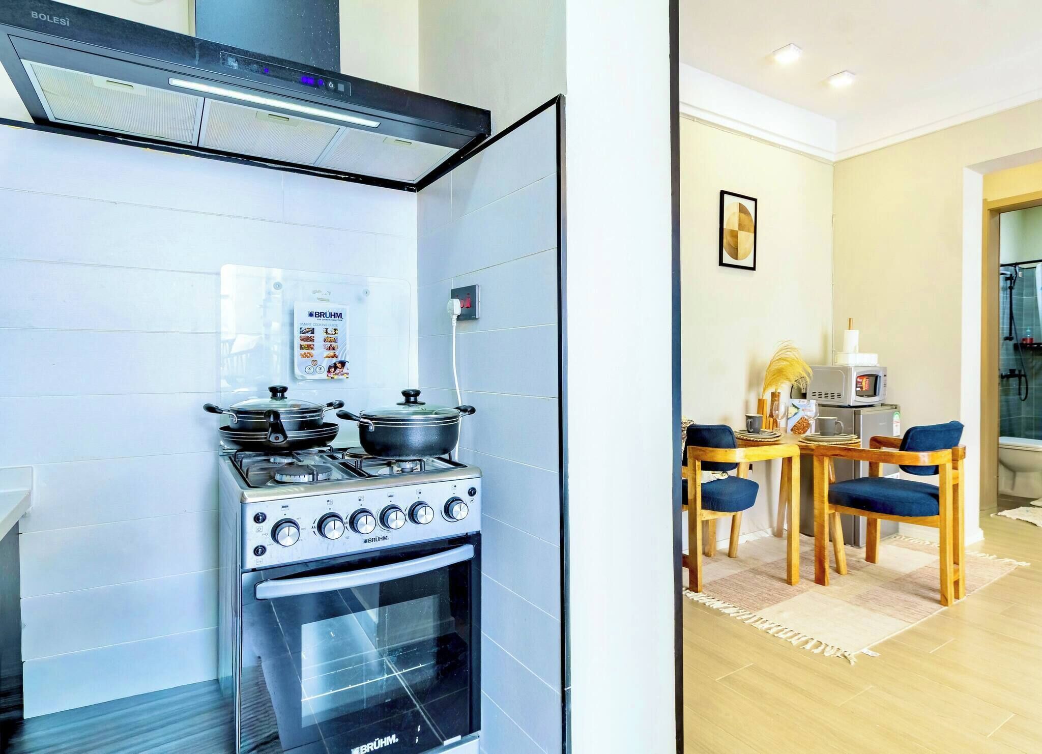 Una cocina compacta con estufa, horno y un dispositivo montado en la pared. Junto a ella, un comedor con mesa, sillas y microondas.