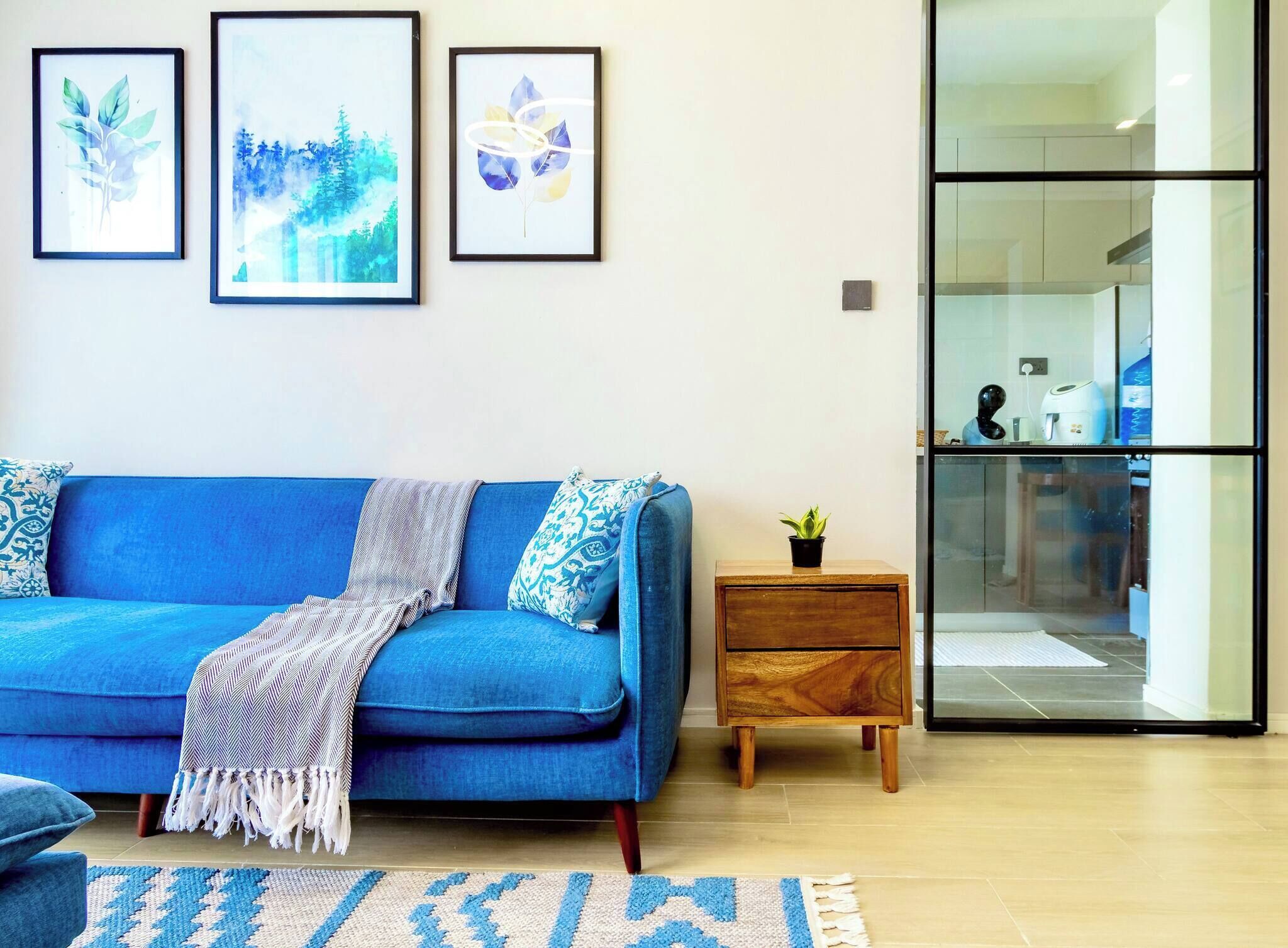 Una sala de estar moderna con un sofá azul, una mesita de madera y un ventanal que da a una cocina.