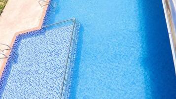 Una piscina rectangular con superficie de agua azul cristalina, rodeada por una terraza de concreto.