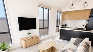 Un salon moderne comprenant un canapé, une table basse, un téléviseur et un coin cuisine avec des meubles en bois et un plan de travail noir.