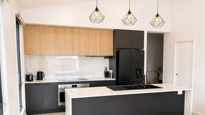 Une cuisine moderne dotée d’un îlot central, de meubles de couleur sombre et d’un éclairage suspendu.