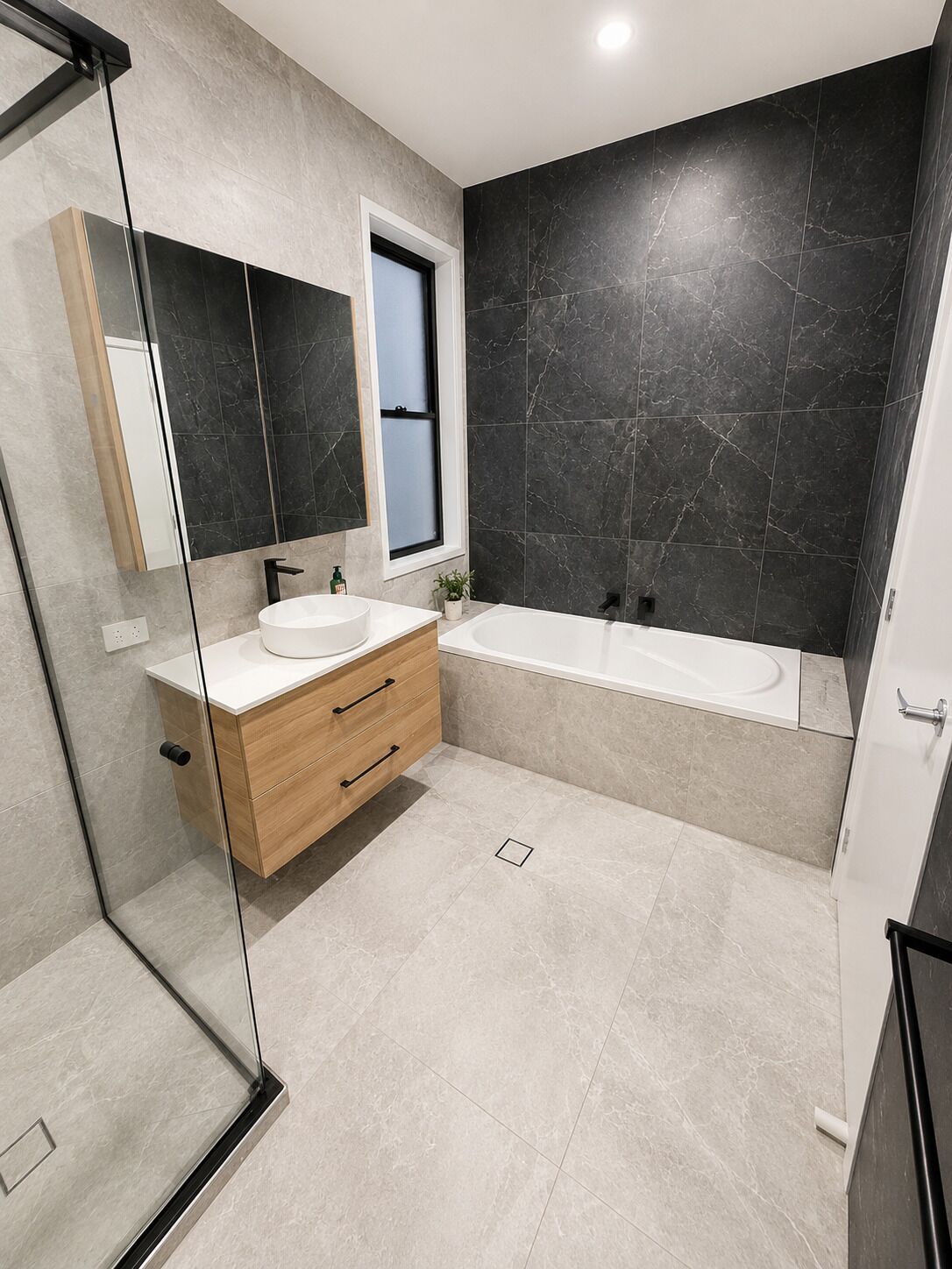 A modern bathroom with a glass shower enclosure, a wooden vanity with a sink, a large mirror, and a bathtub.