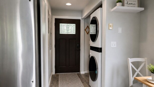 A hallway with a stainless steel refrigerator, a dark door, a wall-mounted laundry machine, and a small table with a chair. - `Reflection`s Edge` Lake House & Private Dock! (Port Angeles)
