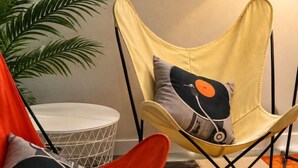 A room with a window, a chair with a vinyl record cushion, a plant, and a patterned rug. - `Reflection`s Edge` Lake House & Private Dock! (Port Angeles)