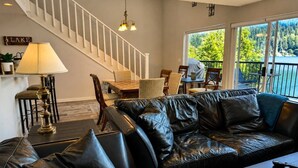 A modern living room with a leather sofa, a dining table, and a staircase. - `Reflection`s Edge` Lake House & Private Dock! (Port Angeles)
