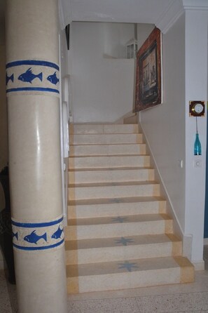 A staircase with beige steps and blue star patterns, leading to a landing with a clock and a framed picture on the wall. - Tigmino is a 5-minute walk from the sea along the cliffs (Mirleft)