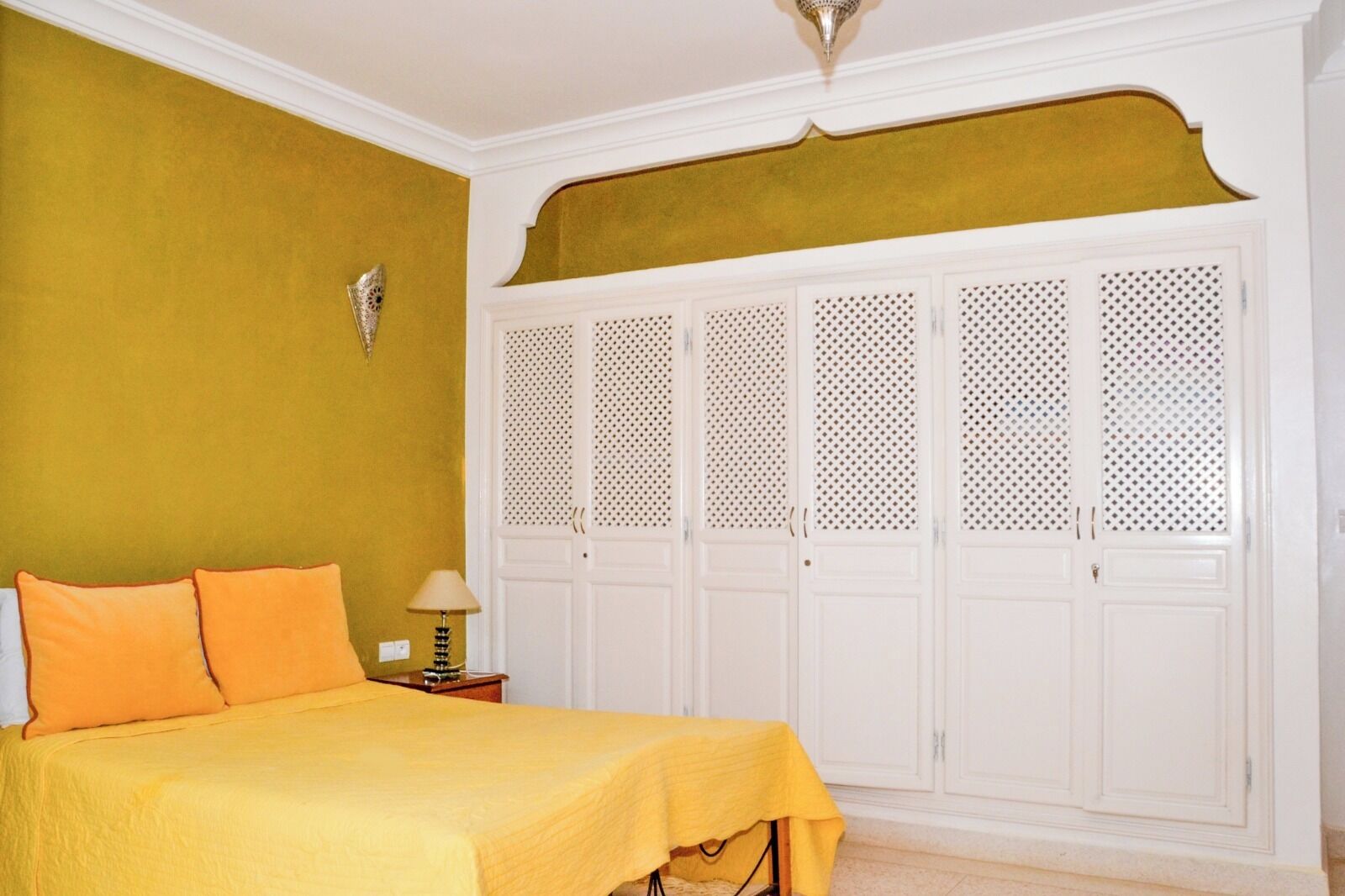 Een slaapkamer met een bed, nachtkastje, lamp en een garderobe met verstelbare deuren.