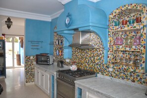 A kitchen with blue walls, a tiled backsplash, and a variety of kitchen appliances including a stove, oven, and microwave. - Tigmino is a 5-minute walk from the sea along the cliffs (Mirleft)