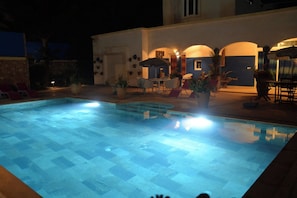 Una piscina con un borde empedrado, rodeada de sillas y mesas de descanso.