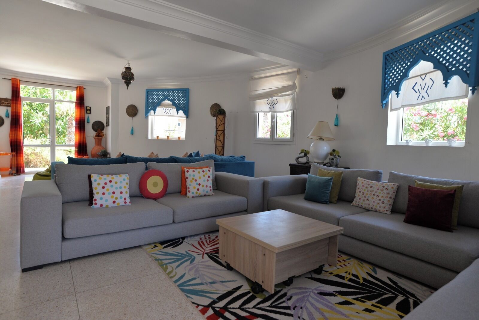 Ein Wohnzimmer mit grauem Sofa, bunten Kissen, einem Holztisch und gemusterten Teppichen.
