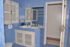 A bathroom with blue tiled walls, a white sink, a mirror, and a toilet. - Vrbo Property (Mirleft)