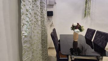 A dining area with a table, chairs, a vase with flowers, a hanging plant, and an air conditioning unit on the wall.