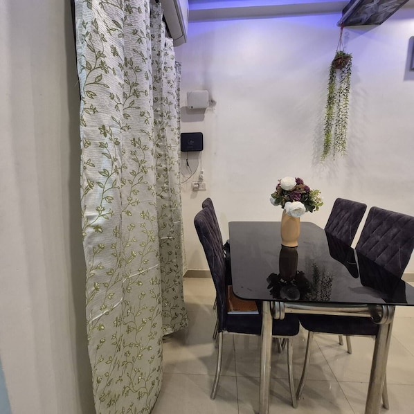 A dining area with a table, chairs, a vase with flowers, a hanging plant, and an air conditioning unit on the wall.