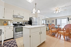 A modern kitchen with white cabinetry, stainless steel appliances, and a central island. - Windy Village OceanView Gem | 2BR Beach Getaway (North Myrtle Beach)
