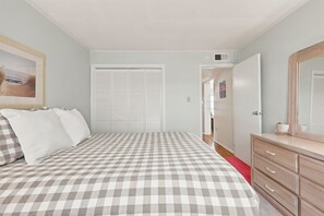 Ein Schlafzimmer mit kariertem Bettbezug, einem Schminktisch, einem Spiegel und einer Tür zu einem anderen Raum.