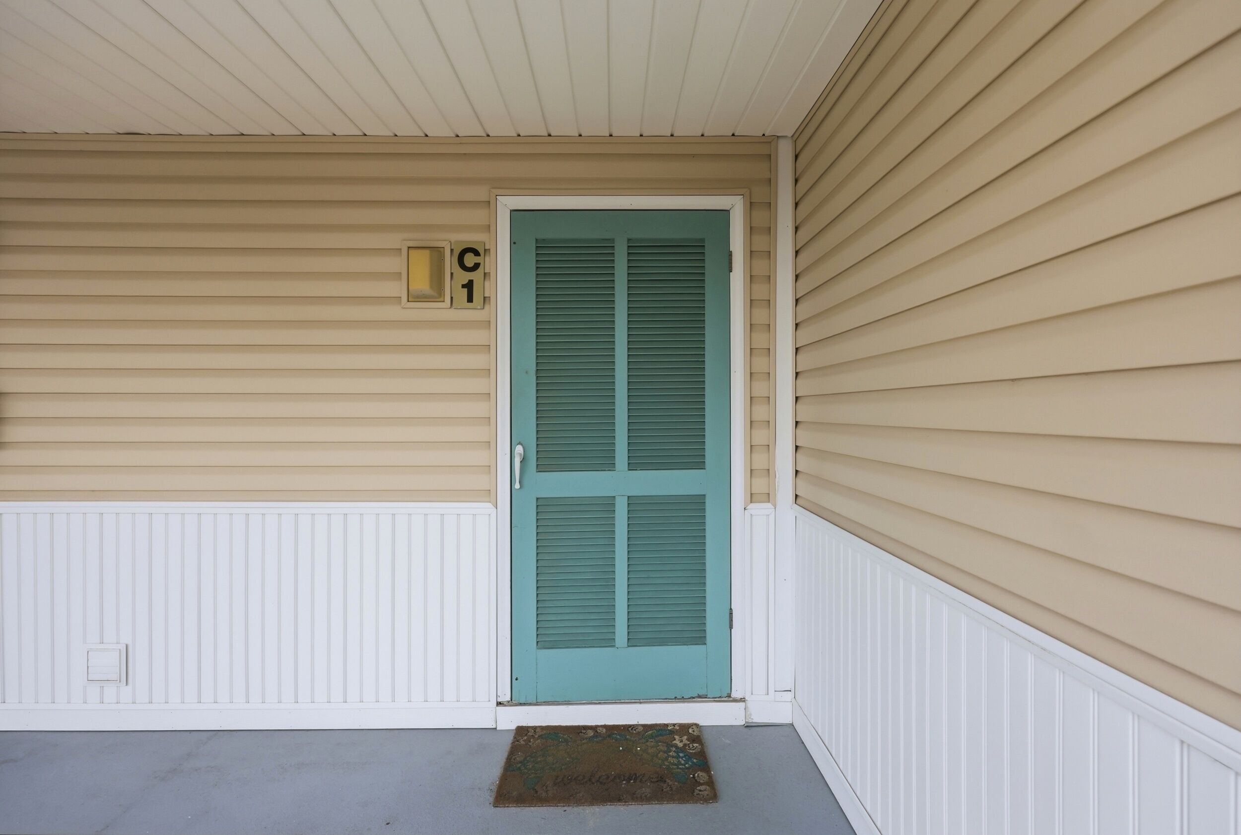 A front porch with a teal door, beige siding, and a white entryway.