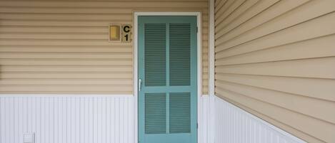 A front porch with a teal door, beige siding, and a white entryway.