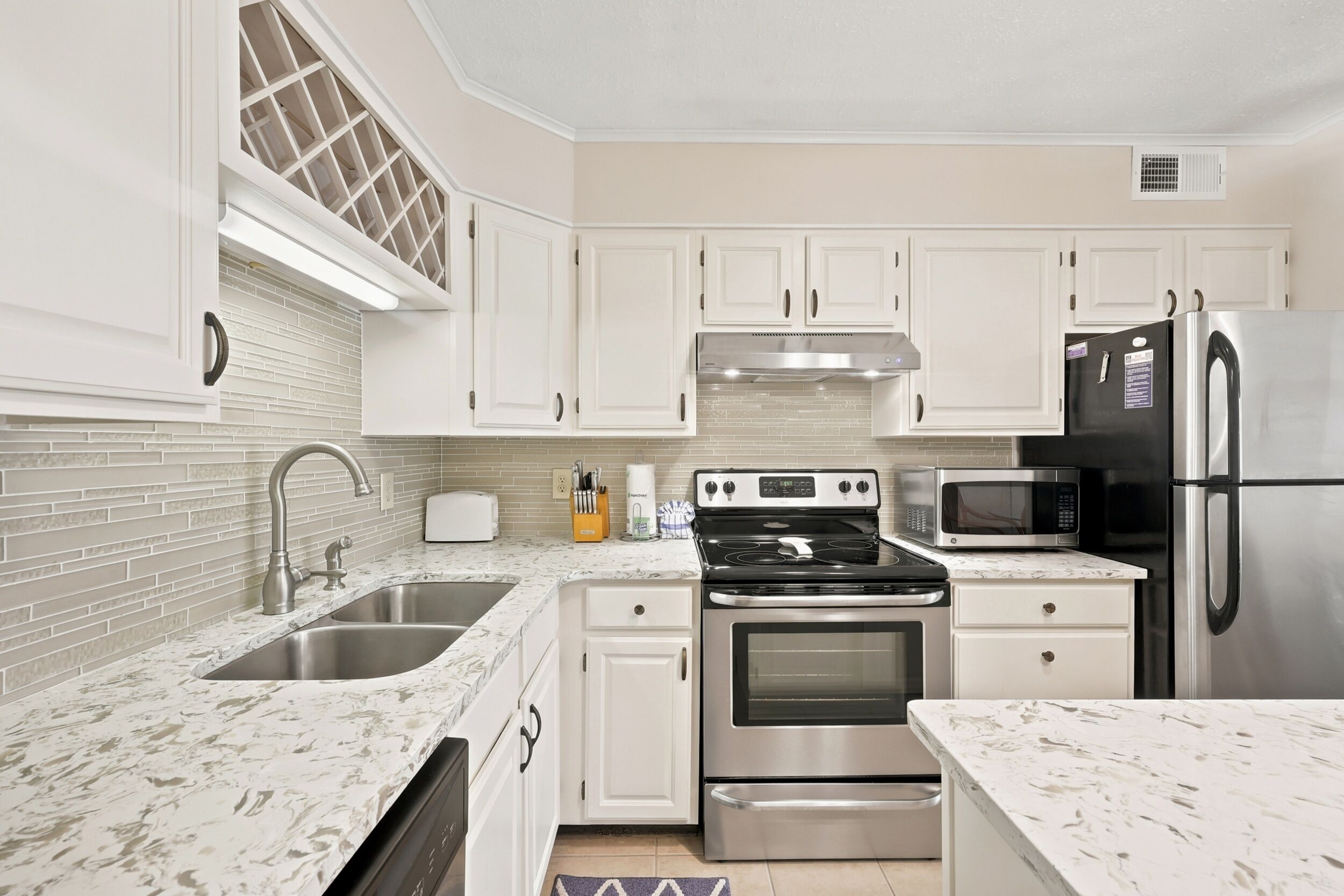 A modern kitchen with white cabinets, a stainless steel refrigerator, a microwave, a stove, and a sink.