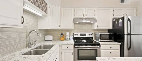 A modern kitchen with white cabinets, a stainless steel refrigerator, a microwave, a stove, and a sink.