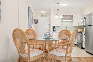 A modern kitchen with white cabinets, stainless steel appliances, and a glass dining table with wicker chairs. - Windy Village OceanView Gem | 2BR Beach Getaway (North Myrtle Beach)