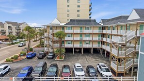 A multi-story motel with a parking lot, several vehicles, and a clear sky. - Windy Village OceanView Gem | 2BR Beach Getaway (North Myrtle Beach)