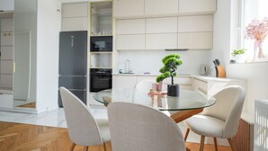A modern kitchen with white cabinetry, a glass dining table, and a potted bonsai tree. - Starowiejska Baltic Comfort Apartment (Gdańsk)