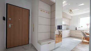 A modern interior with a wooden door, a built-in bench with storage, a kitchen area, and a dining space. - Starowiejska Baltic Comfort Apartment (Gdańsk)