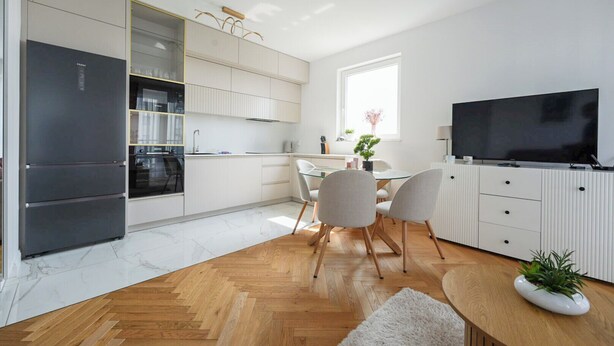 A modern kitchen with a built-in refrigerator, a dining area with a glass table, and a television on the wall. - Starowiejska Baltic Comfort Apartment (Gdańsk)