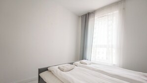 A minimalist bedroom with a bed, a window with sheer curtains, and a plain wall. - Starowiejska Baltic Comfort Apartment (Gdańsk)