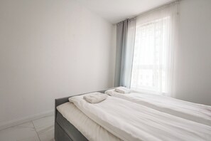 Une chambre à coucher au style minimaliste, avec un lit, une fenêtre ornée de rideaux légers et un mur uni.