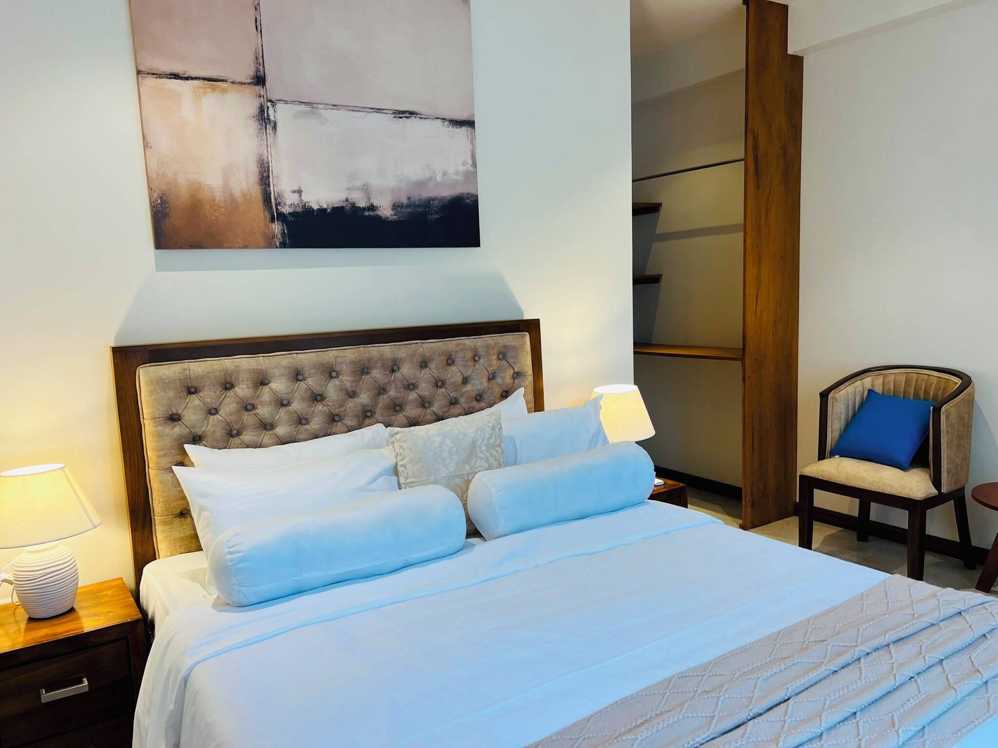 A hotel room with a large bed, a nightstand, a chair, and a wall-mounted abstract painting.