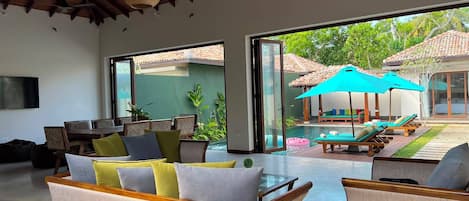 A spacious living area with a large TV, comfortable seating, and a view of a pool and outdoor furniture.